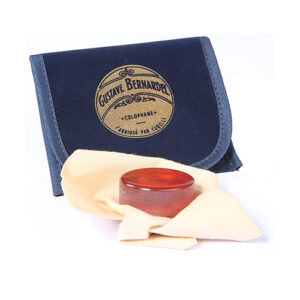A round piece of amber-colored rosin on a beige cloth is placed in front of a navy blue Gustave Bernardel branded case with gold and black lettering.